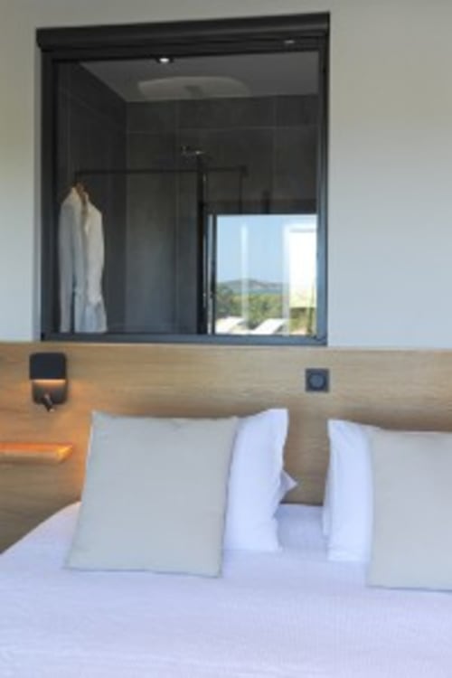 Chambre moderne à la Villa Poggioli avec literie blanche, tête de lit en bois et baie vitrée vue mer à Zonza, Corse