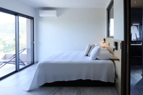Chambre de villa moderne avec balcon vue mer, lit blanc, table de nuit en bois et climatisation aux Villas d'A Storia