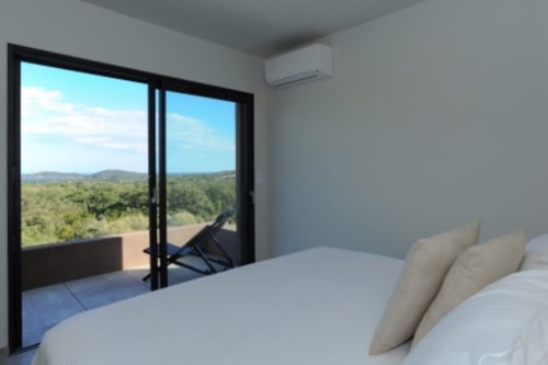Chambre moderne de la Villa Poggioli, Zonza, avec vue sur la mer par portes vitrées sur le paysage méditerranéen