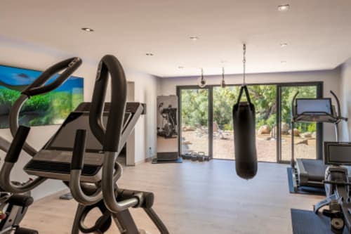 Salle de sport moderne à la Villa Poggioli des Villas d'A Storia avec vélo d'exercice, sac de frappe, tapis roulant et vue sur le jardin