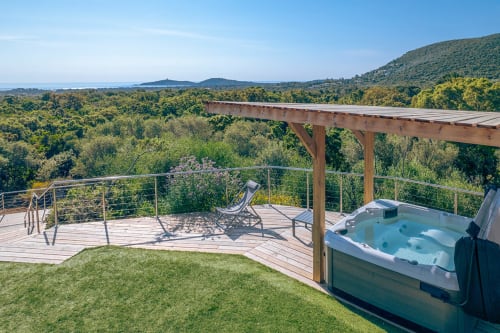 Villa Poggioli aux Villas d'A Storia à Zonza avec bain à remous, terrasse, transat et vue mer sur paysage boisé.