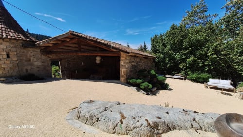 Cour du Furanelle B&B à Saint Etienne : bâtiments en pierre, sol sableux et verdure luxuriante sous ciel bleu dégagé