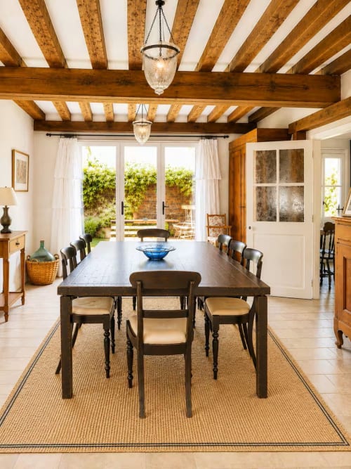 Spacieuse salle à manger aux poutres apparentes, table noire et portes-fenêtres donnant sur le jardin du gîte Les Maraîchades