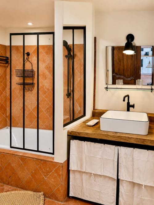 Salle de bain élégante aux carreaux en terre cuite, douche à cadre noir, vasque blanche et meuble de salle de bain en bois aux Maraîchades