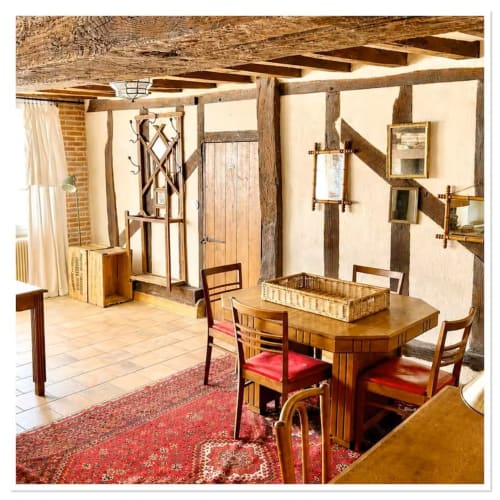 Intérieur rustique du cottage Les Maraîchades avec poutres en bois, table à manger, tapis rouge et murs en pierre apparente en Sologne,