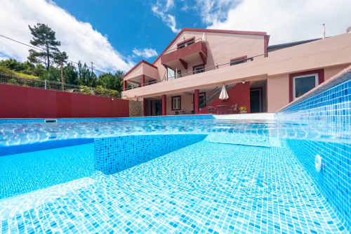 Luxury villa in Prazeres with sparkling blue swimming pool, red-accented modern architecture, mountain views, and lush