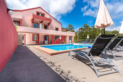 Pink villa with swimming pool, loungers, and white umbrellas in Prazeres, Portugal