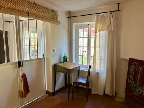 Intérieur lumineux du gîte Les Maraîchades avec bureau, chaise, vue sur jardin par portes-fenêtres et rideaux crème