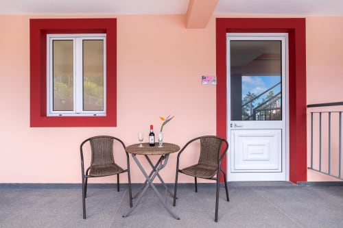 Pink terrace at Garry's Holiday Rentals villa in Prazeres with wicker chairs, round table, and mountain views through