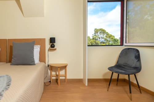 Modern bedroom in Prazeres villa with wooden bed, mountain view windows, black chair, and wooden flooring