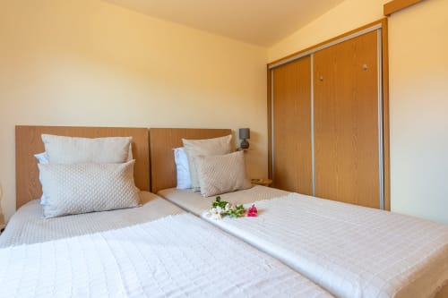 Bright bedroom in Prazeres villa with two beds, wooden headboards, white bedding, and mountain views through windows