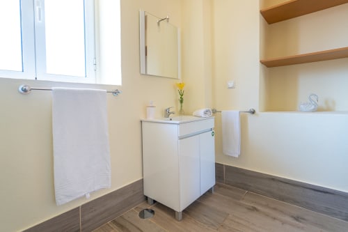 Modern bathroom in Quinta frizado villa with white vanity, mirror, towel rails, yellow walls, wooden flooring, and shelving