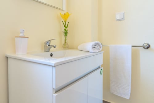 Modern bathroom vanity with white sink, chrome faucet, towel rack, and yellow flower vase at Garry's Holiday Rentals villa in