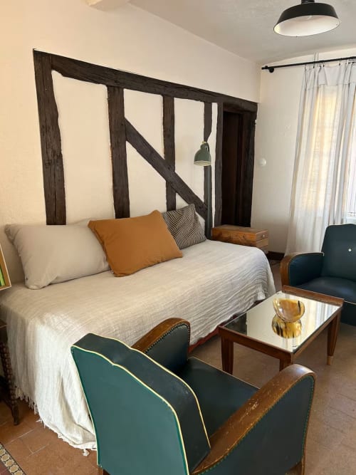 Chambre du gîte Les Maraîchades avec tête de lit en bois, literie crème, fauteuil bleu canard et vue sur le jardin en Sologne