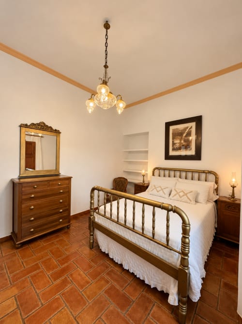 Elegante dormitorio en Casa Rural Garden Suites de Xàtiva con cama de latón, muebles de madera, piso de terracota y lámpara colgante
