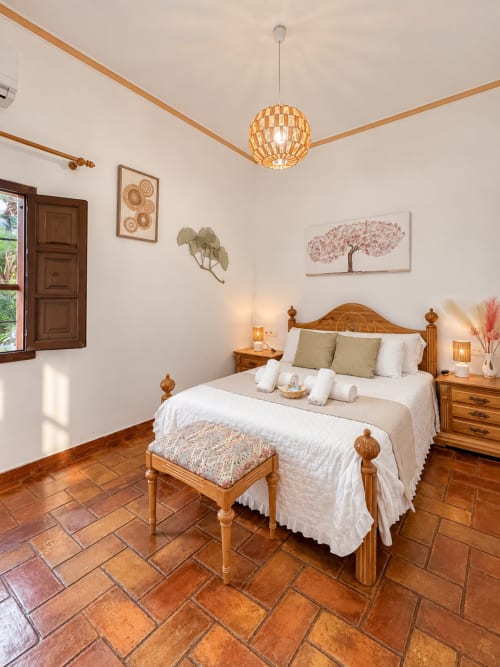 Dormitorio luminoso con cama de madera, suelos de barro y lámpara tejida en Casa Rural Garden Suites, Xàtiva