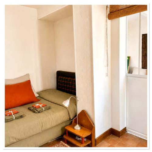 Chambre douillette du gîte Les Maraîchades en Sologne avec literie beige, coussin orange, table de nuit en bois et vue sur le jardin