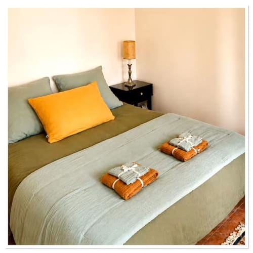 Chambre accueillante au gîte Les Maraîchades en Sologne avec parure olive, coussin orange et serviettes de bienvenue
