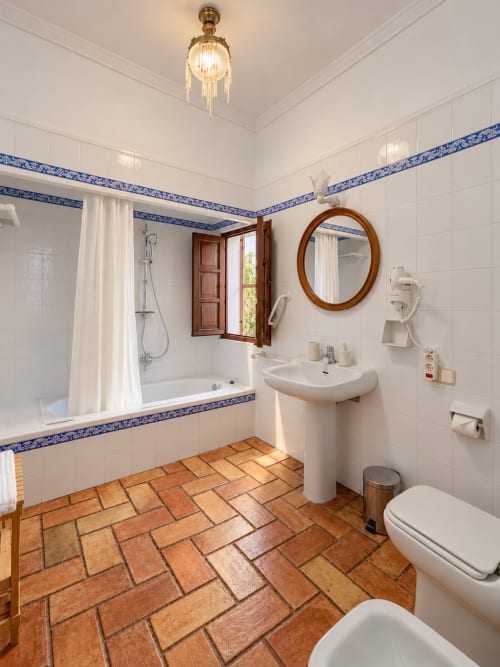 Baño elegante en Casa Rural Garden Suites de Xàtiva con azulejos blancos, cenefa azul decorativa, suelo de barro y lavabo pedestal