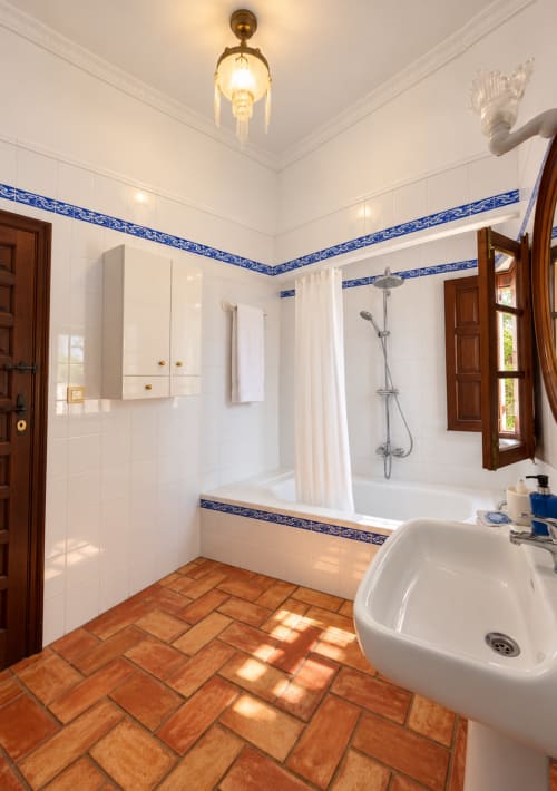 Elegante baño en Casa Rural Garden Suites de Xàtiva con azulejos blancos, detalles azules, piso de terracota, bañera y ducha