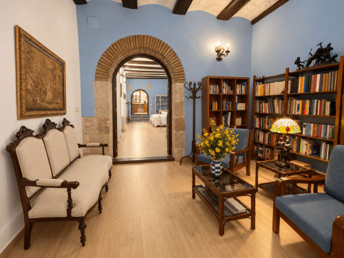 Elegante sala de lectura en Casa Rural Garden Suites, Xàtiva, con estanterías de madera, muebles ornamentales y paredes azules