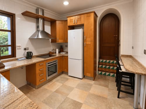 Cocina moderna con muebles de madera, encimeras de granito y electrodomésticos de acero inoxidable en Casa Rural Garden Suites