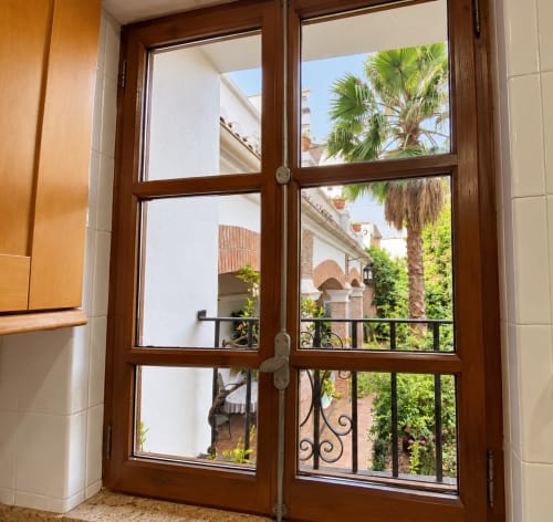 Puertas francesas de madera que abren a un patio ajardinado con palmeras y arquitectura histórica en Casa Rural Garden Suites