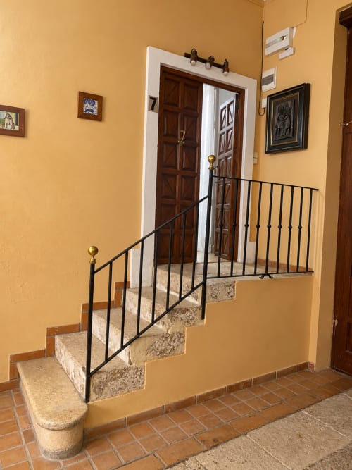Escalera con barandilla de metal negro que conduce a puertas de madera en pasillo de paredes amarillas en Casa Rural Garden Suites, Xàtiva