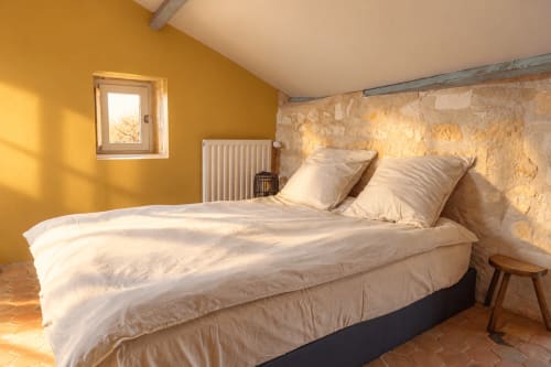 Chambre lumineuse du gîte Le Clos Divin à Doué-la-Fontaine, murs en pierre, touches de jaune et literie blanche