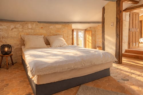 Chambre lumineuse du gîte Maison Minérale au Clos Divin avec murs en pierre, poutres en bois et carrelage en terre cuite