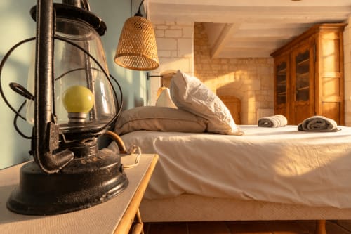 Chambre rustique au gîte Le Clos Divin avec lanterne vintage, luminaire suspendu tressé et literie blanche, vue sur le jardin