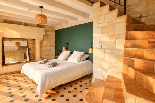 Chambre Maison Minérale au Clos Divin : murs en pierre, tête de lit verte, linge blanc, carrelage terracotta
