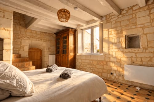 Chambre lumineuse en pierre au gîte Le Clos Divin à Doué-la-Fontaine avec poutres apparentes, mobilier bois et lumière du jardin