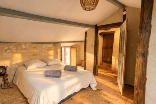Chambre rustique du gîte Le Clos Divin avec murs en pierre, poutres en bois, literie blanche et carrelage en terre cuite