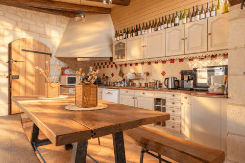 Cuisine rustique au Clos Divin avec poutres en bois, placards crème, vitrine à vin et table à manger en bois.