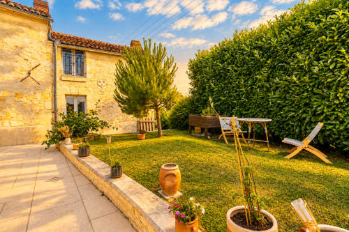 Vue ensoleillée du jardin du gîte Le Clos Divin à Doué-la-Fontaine avec maison en pierre, terrasse, pelouse et mobilier extérieur