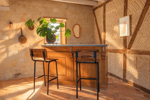 Espace de travail en pierre rustique au Clos Divin avec bureau en bois, tabourets de bar et plantes en pot à Doué-la-Fontaine