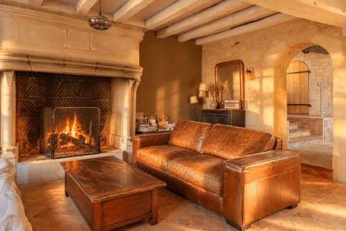 Salon chaleureux du gîte Le Clos Divin avec cheminée, canapé en cuir et poutres en bois à Doué-la-Fontaine