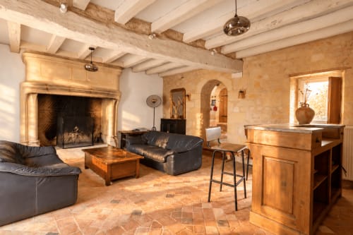 Salon rustique en pierre du Clos Divin avec cheminée, plafond à poutres, carrelage en terre cuite et mobilier contemporain
