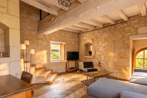 Intérieur spacieux du cottage en pierre du Clos Divin avec poutres apparentes, mobilier bois, téléviseur et vue sur le jardin par des arcades