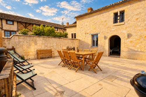 Cour ensoleillée de la maison d'hôtes Le Clos Divin à Doué-la-Fontaine avec mobilier de jardin en bois et chaises longues