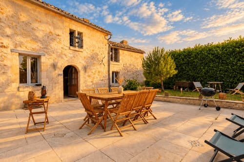 Terrasse ensoleillée du cottage Le Clos Divin à Doué-la-Fontaine avec mobilier de jardin en bois et villa en pierre