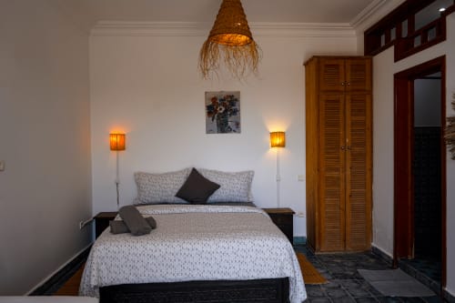 Lazulite bedroom at Imsouane Surf Paradise with ocean view, woven pendant lamp, warm wall sconces, and wooden wardrobe