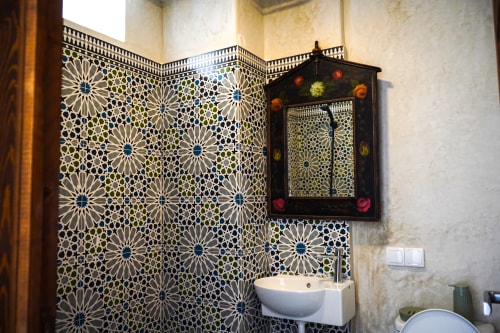 Moroccan bathroom with geometric zellige tilework, decorative mirror, and white sink at Imsouane Surf Paradise