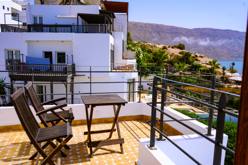 Sunny terrace at Imsouane Surf Paradise with wooden chairs, table, sea view balcony, and Atlas Mountains backdrop in Agadir,