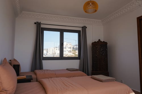 Tagante room at Imsouane Surf Paradise with sea view, twin beds, wooden wardrobe, and balcony overlooking Agadir buildings