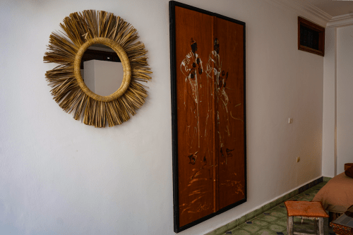 Loubana room at Imsouane Surf Paradise features golden sunburst mirror and traditional Moroccan wood artwork on white walls