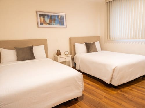 Dormitorio luminoso en Casa Donceles en Ciudad de México con dos camas queen, cabeceras beige, sábanas blancas y detalles de madera