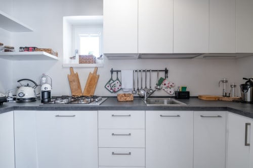 Cucina moderna bianca con fornello a gas, taglieri in legno e lavello in acciaio inox a Villa Casolare Treggi a Ostuni