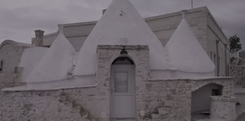 Villa trullo imbiancata a Ostuni con base in pietra, portale ad arco e caratteristico tetto conico